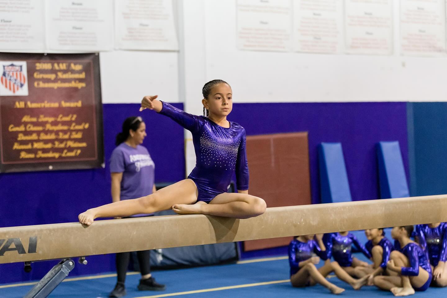 niña practicando split en la viga con su entrenadora